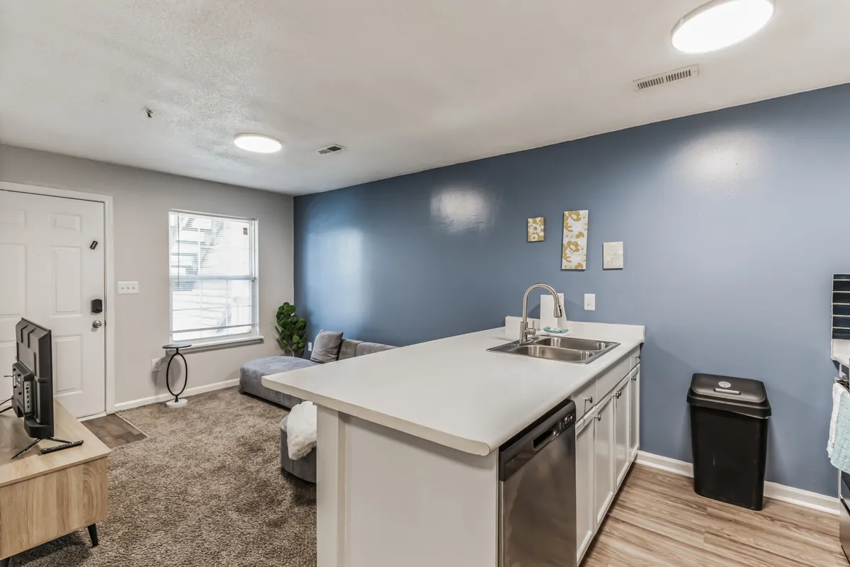 This interior scene captures the kitchen island with a blue accent wall in the background, blending seamlessly into a cozy living area with a couch and television. The open layout reflects a casual, comfortable atmosphere perfect for hosting gatherings, enjoying a quick breakfast, or relaxing after a meal.