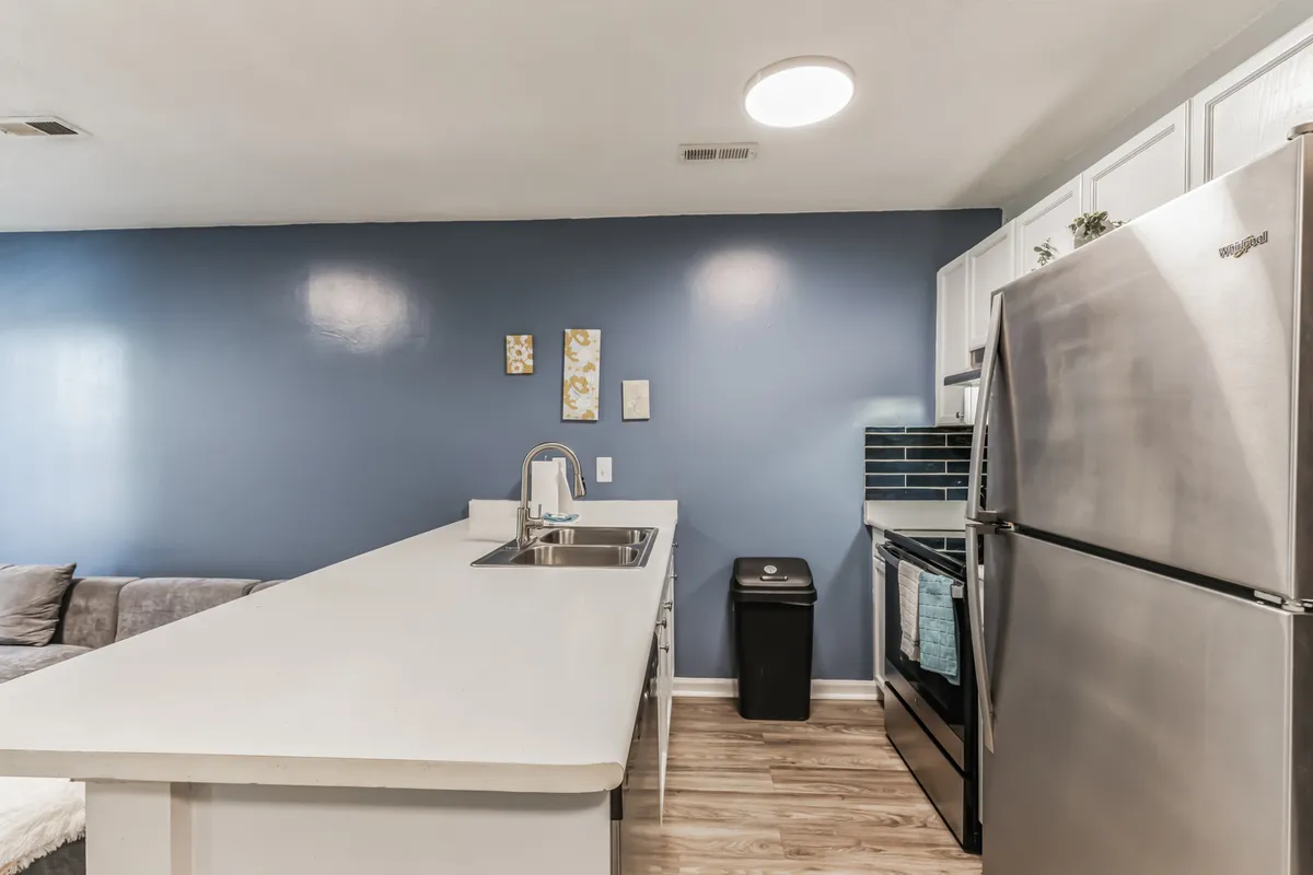 A modern kitchen with a sleek island, stainless steel appliances, and a striking blue accent wall. The layout is welcoming and open, ideal for creating meals or gathering with friends. The kitchen is well-lit and designed for both function and style, hinting at the day-to-day comforts awaiting after urban or nature excursions.