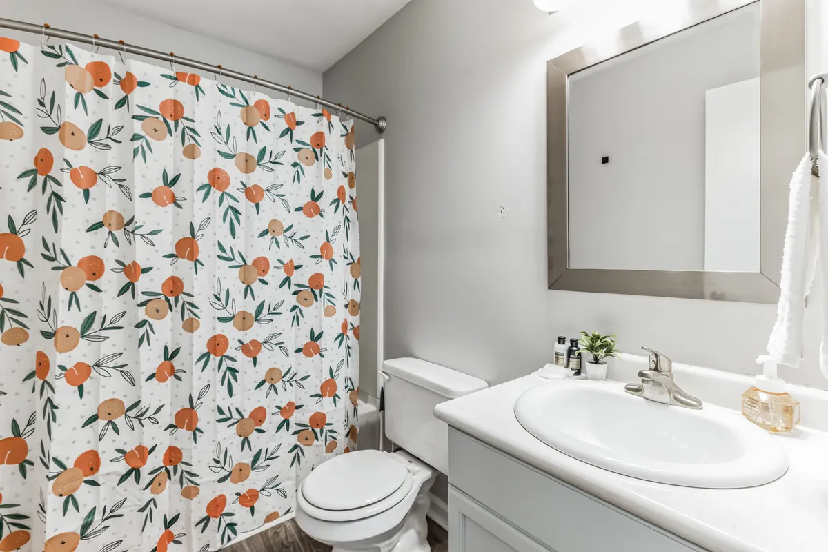 A modern bathroom with a colorful shower curtain, a well-lit vanity with a sink, and a framed mirror. The space feels lively yet cozy, perfect for personal routines or unwinding with a relaxing bath.