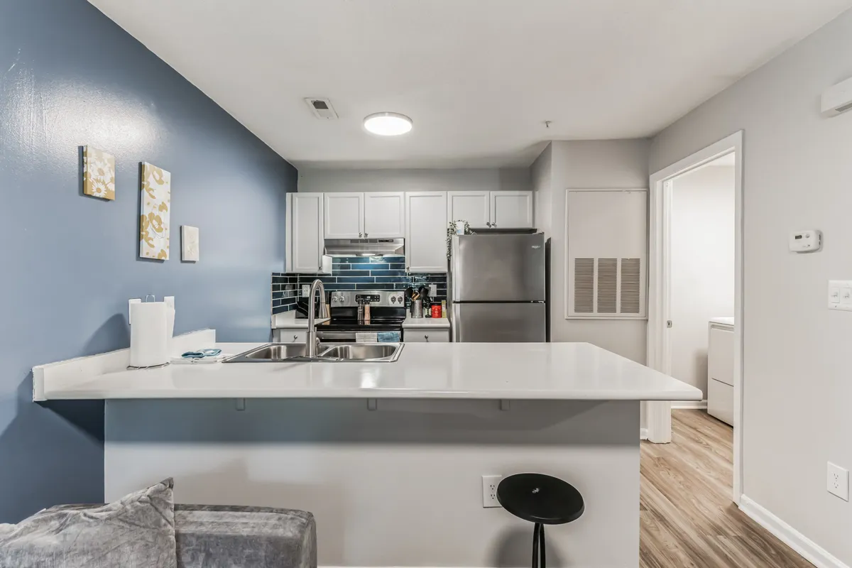 The image shows a spacious kitchen with a central island, stainless steel appliances, a blue accent wall, and decorative wall art. The setting is perfect for both meal preparation and social gatherings, providing ample space for entertaining or sharing meals. Natural light and stylish details add to the kitchen's appeal.