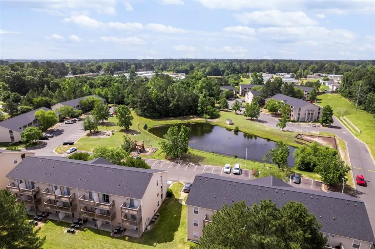 This serene exterior image features apartment buildings set around a tranquil pond with lush green spaces and a dedicated play area. The setting is ideal for outdoor relaxation, family gatherings, or morning jogs, highlighting the natural surroundings and communal amenities.