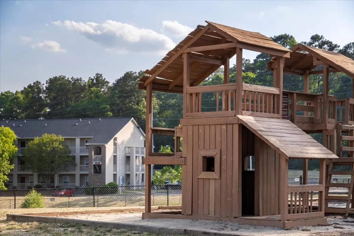 A lively playground is surrounded by greenery and nearby apartment buildings, with children and families enjoying the outdoors. The scene captures joyful moments and the sense of community that comes with family-friendly amenities.